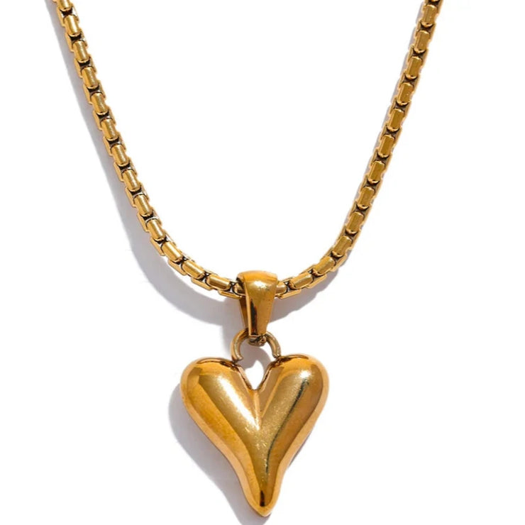 Close-up of a golden heart pendant necklace laid flat on  backdrop.