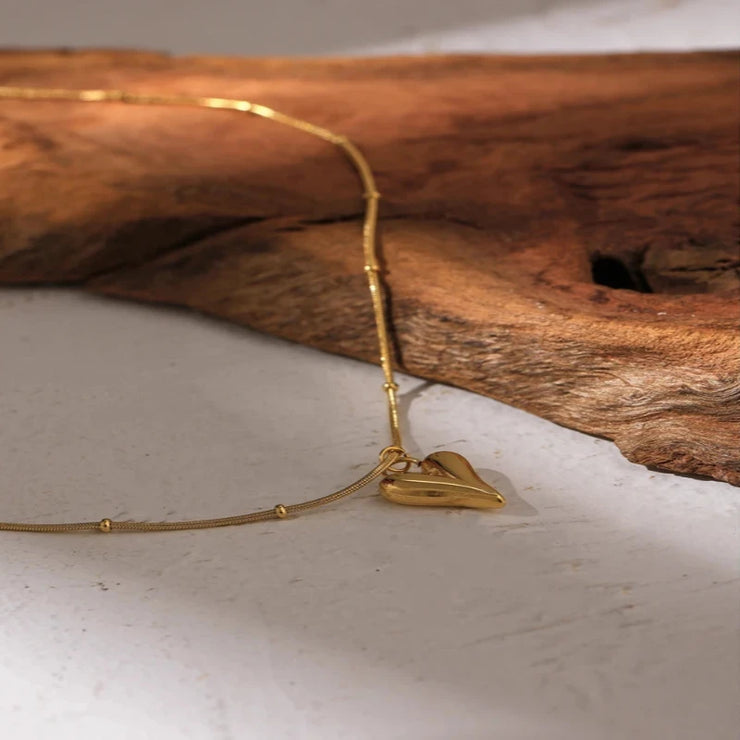  Overhead shot of the heart pendant choker necklace laid flat on a marble surface, showcasing its simplicity.